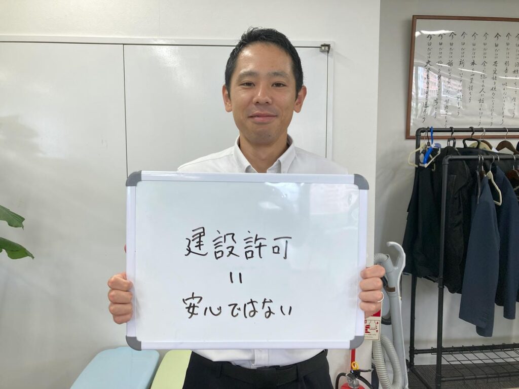 建設業許可について解説し、ホワイトボードを持つ初田理事