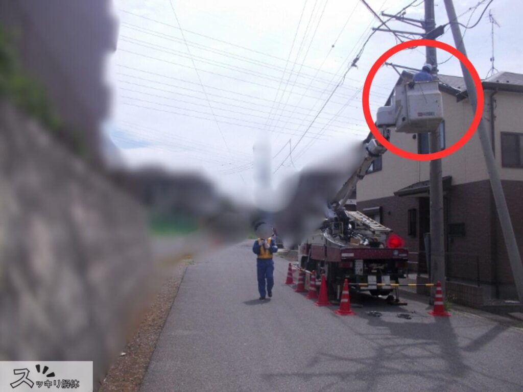 解体工事前の電線撤去作業の様子。送配電会社の作業員が高所作業車を使用し、電柱から建物へ引き込まれた電線を安全に取り外している実際の現場写真。