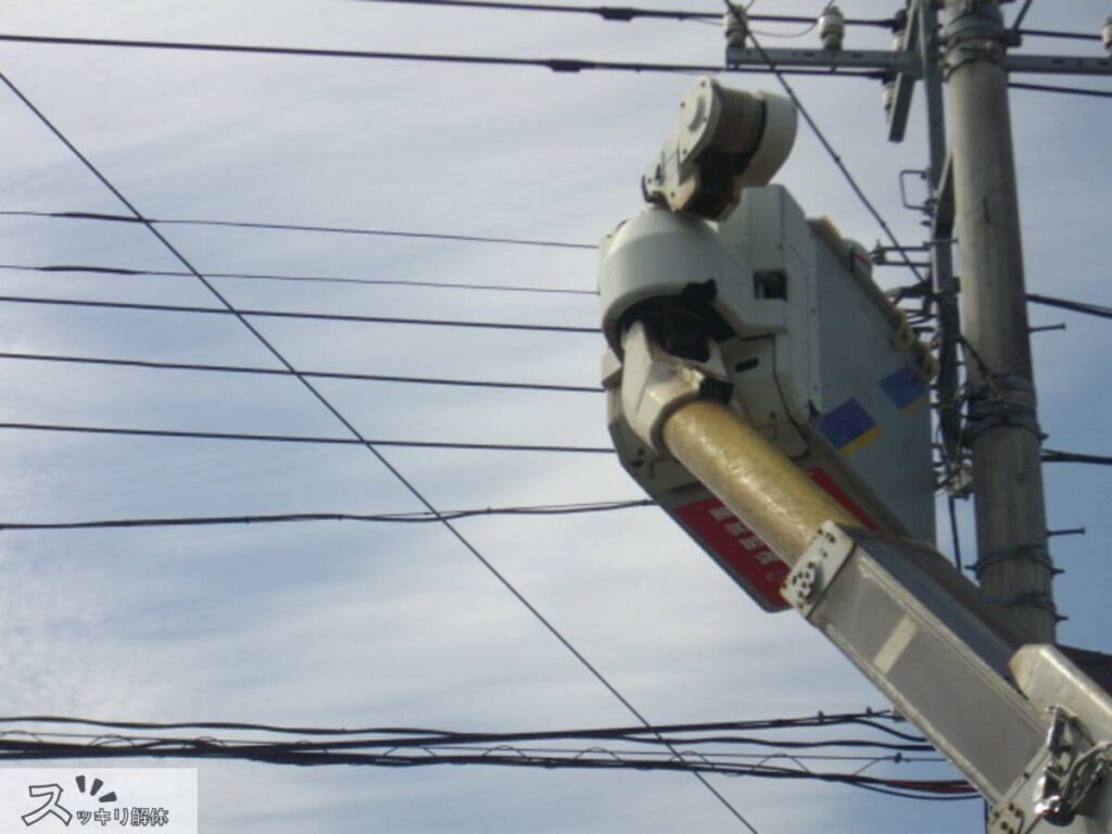 電線撤去の遅延事例における実際の作業現場写真。専門員がバケット車を用いて電柱から建物の引込線を切り離している。